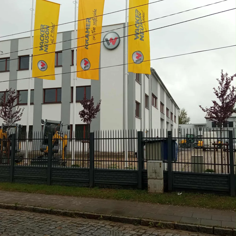 Flagi reklamowe Wacker Neuson przy ogrodzeniu oddziału