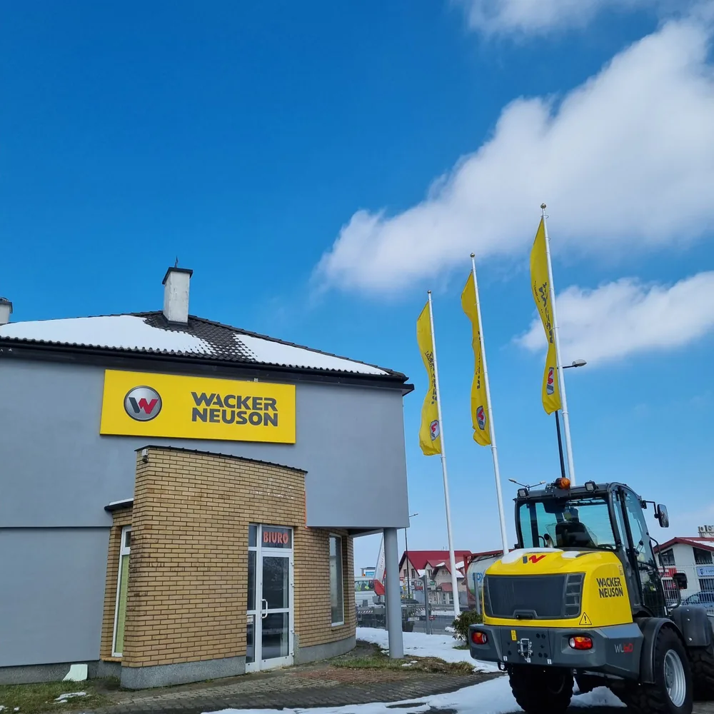Oddział Wacker Neuson z szyldem na elewacji i flagami przy wjeździe